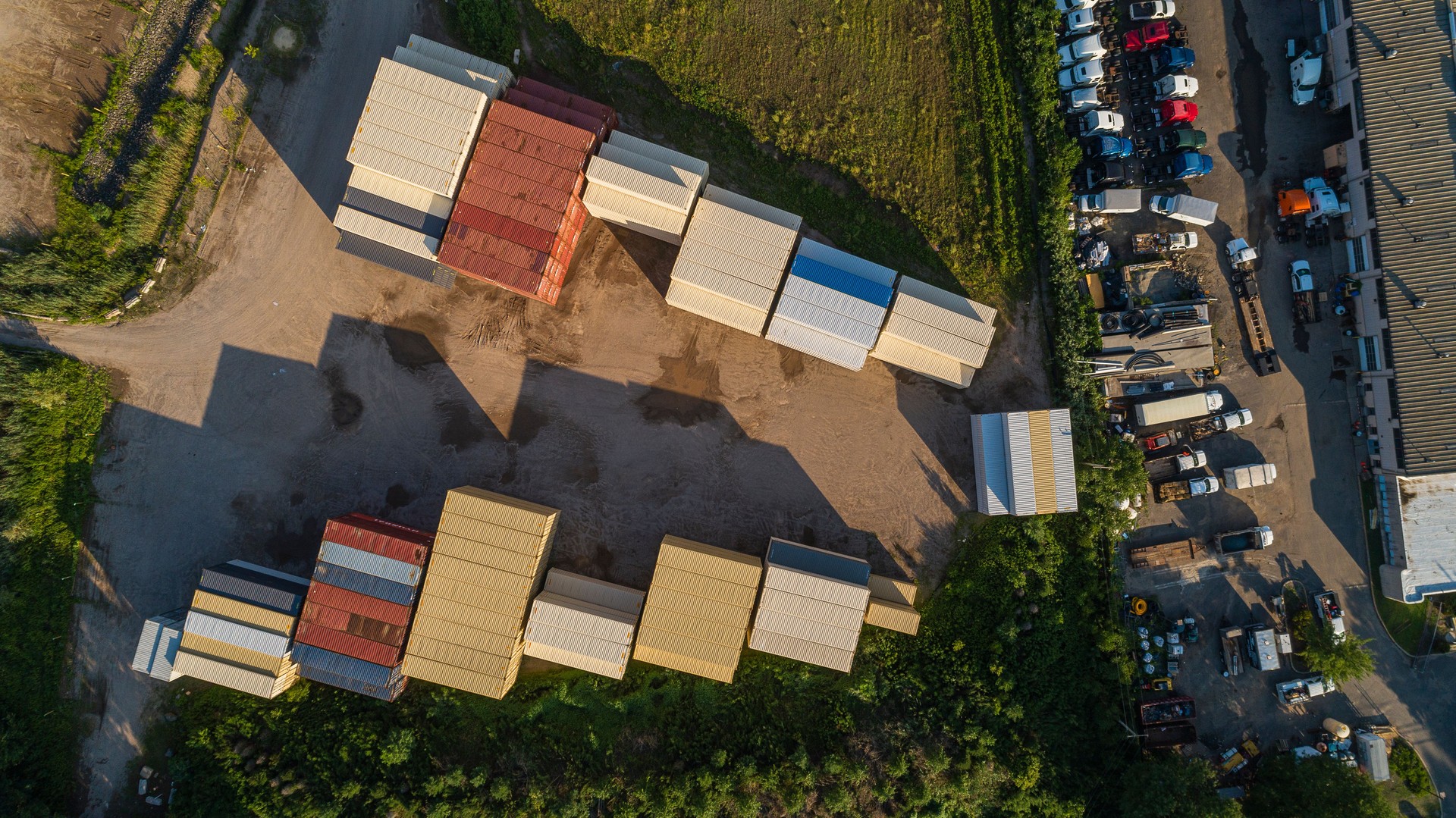 Aerial view of many commercial trucks are parked at the parking lot nearby a warehouse with stockpiled cargo containers.